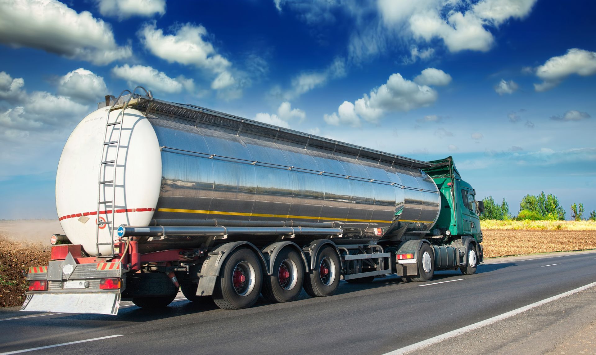A tanker truck is driving down a highway next to a field.