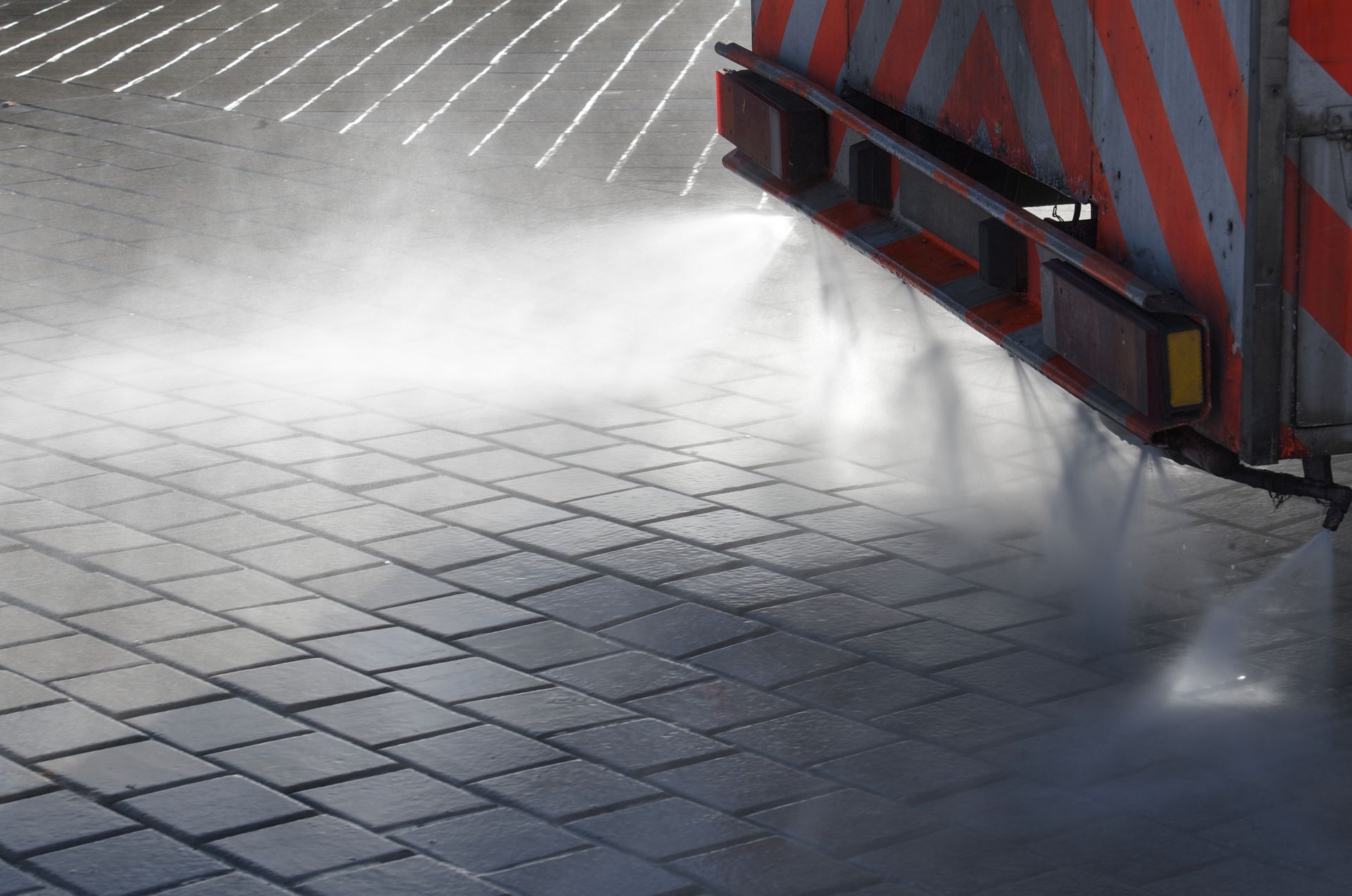 A truck is spraying water on a brick pavement.