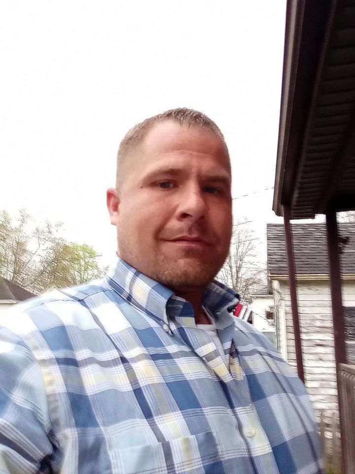 A man in a plaid shirt is standing in front of a house.