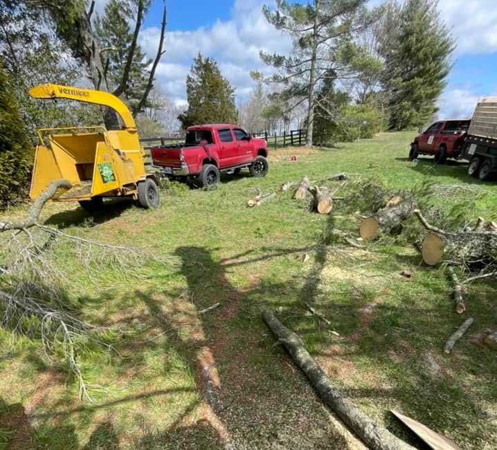 A red truck is parked in a grassy field next to a tree chipper.