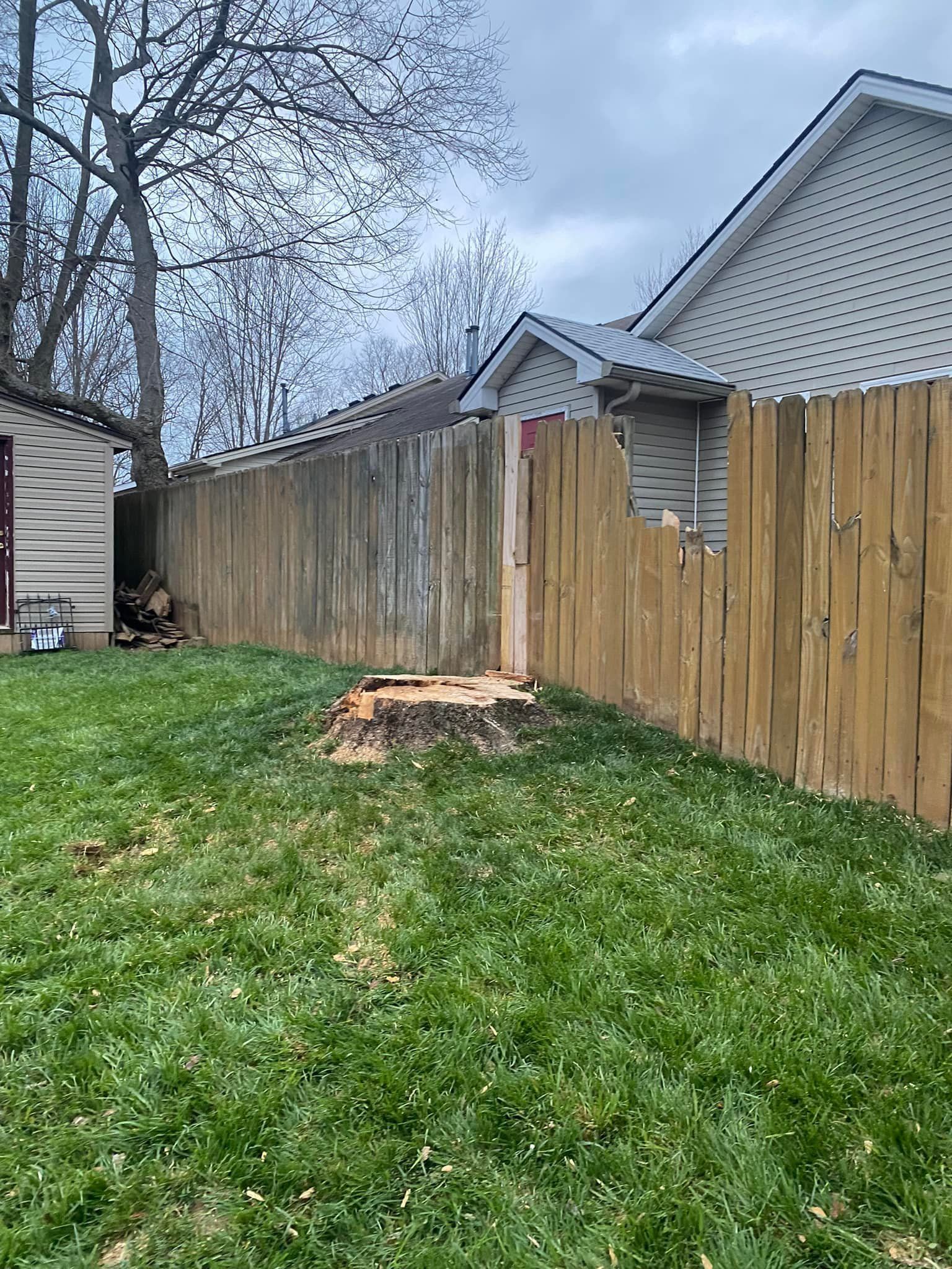 A wooden fence with a tree stump in the grass in front of it.