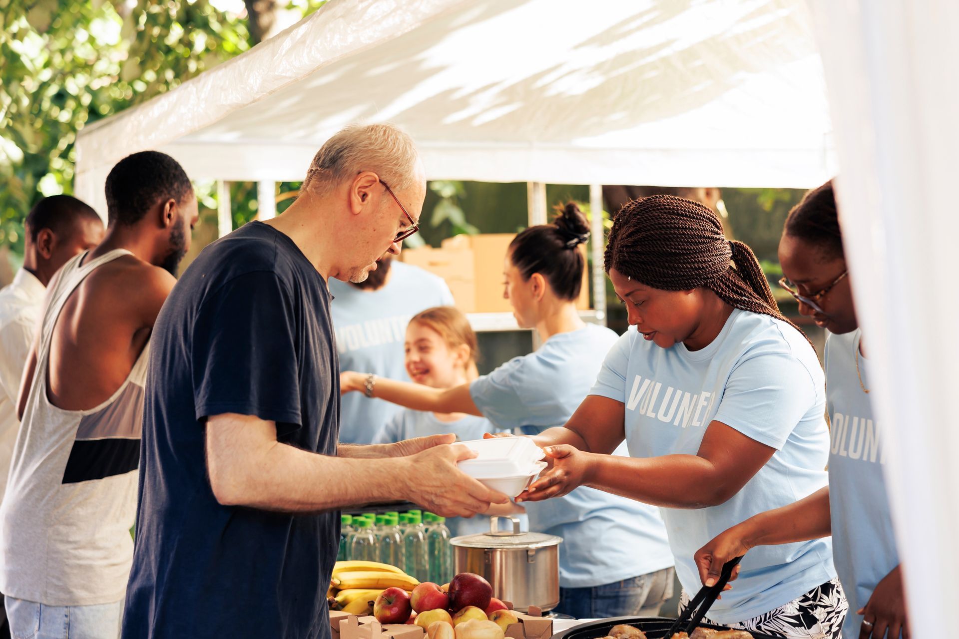 Volunteers serving food at a community outdoor buffet under a white canopy