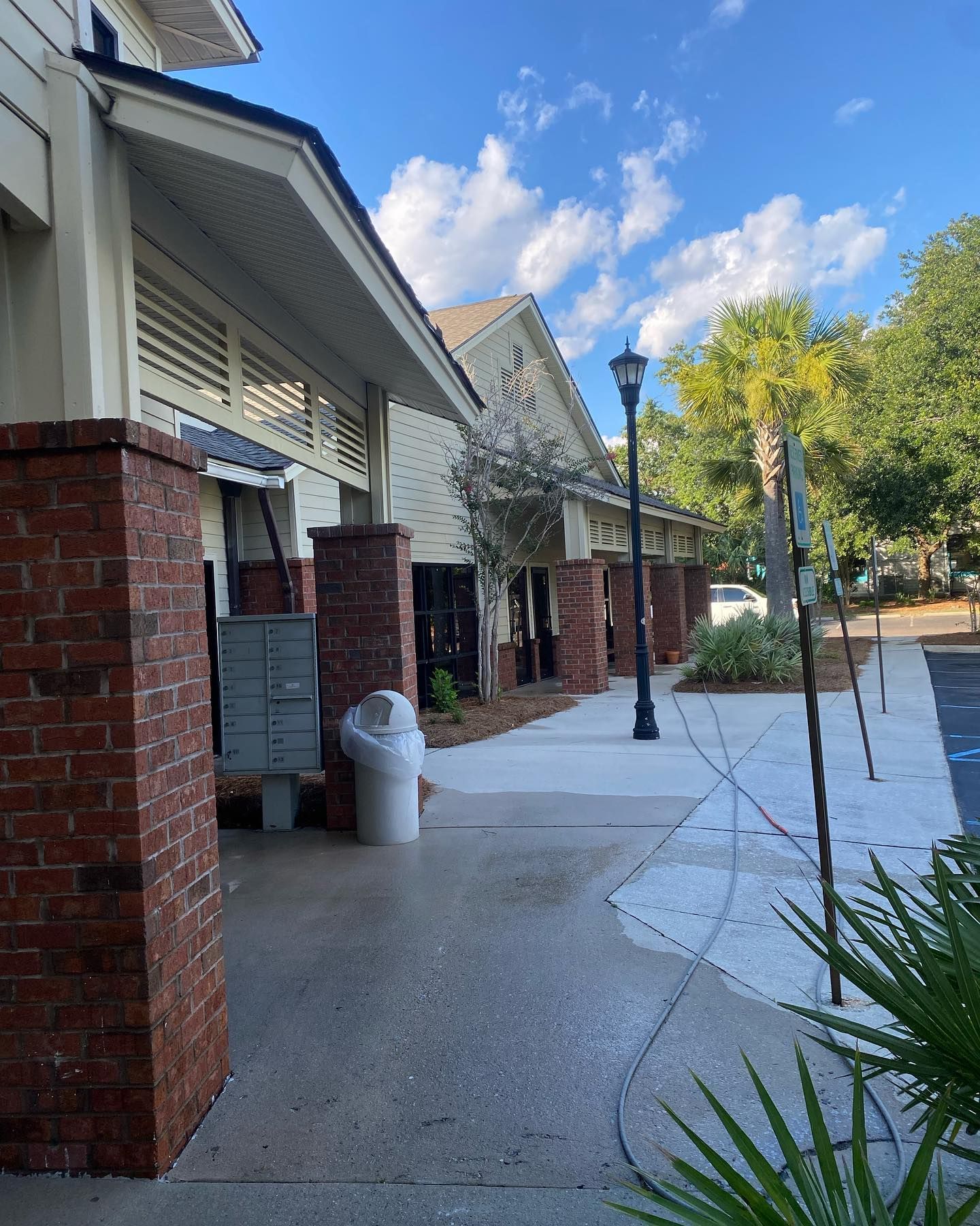 A white trash can is sitting on the sidewalk in front of a brick building.