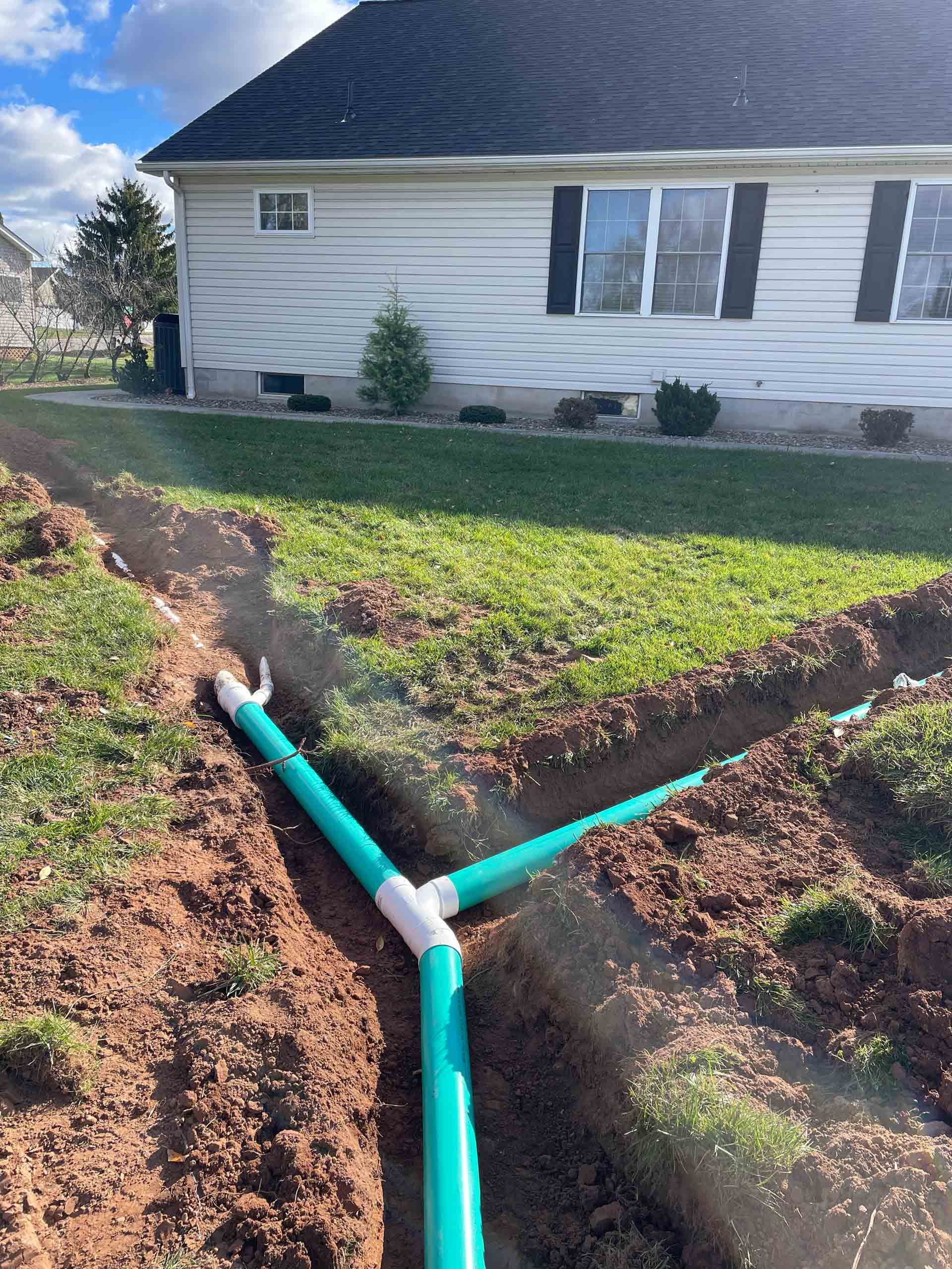 A green pipe is being installed in the dirt in front of a house.