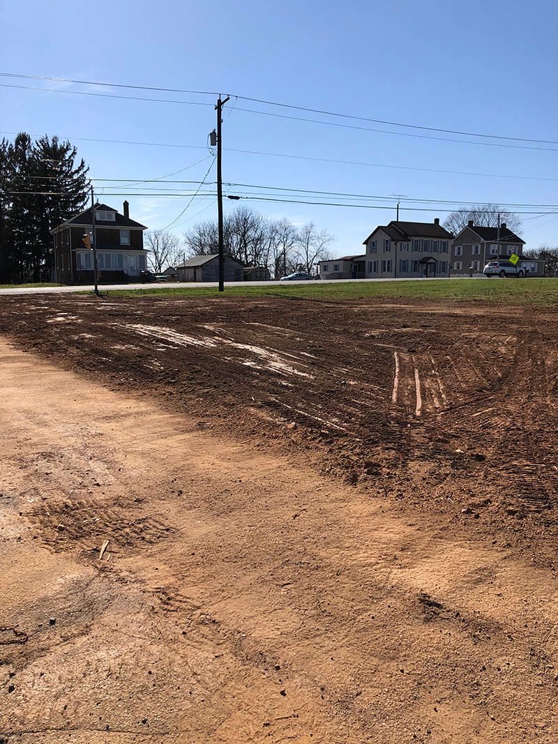 A dirt road going through a field with a house in the background.