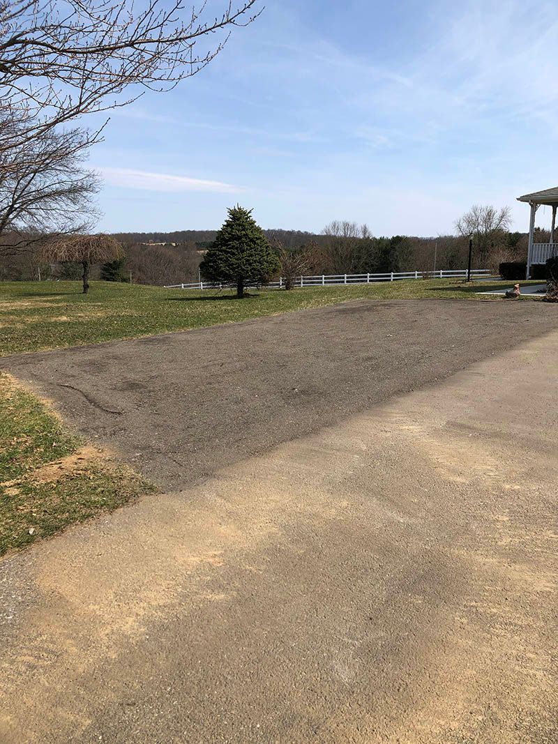 A dirt road going through a grassy field with a house in the background.
