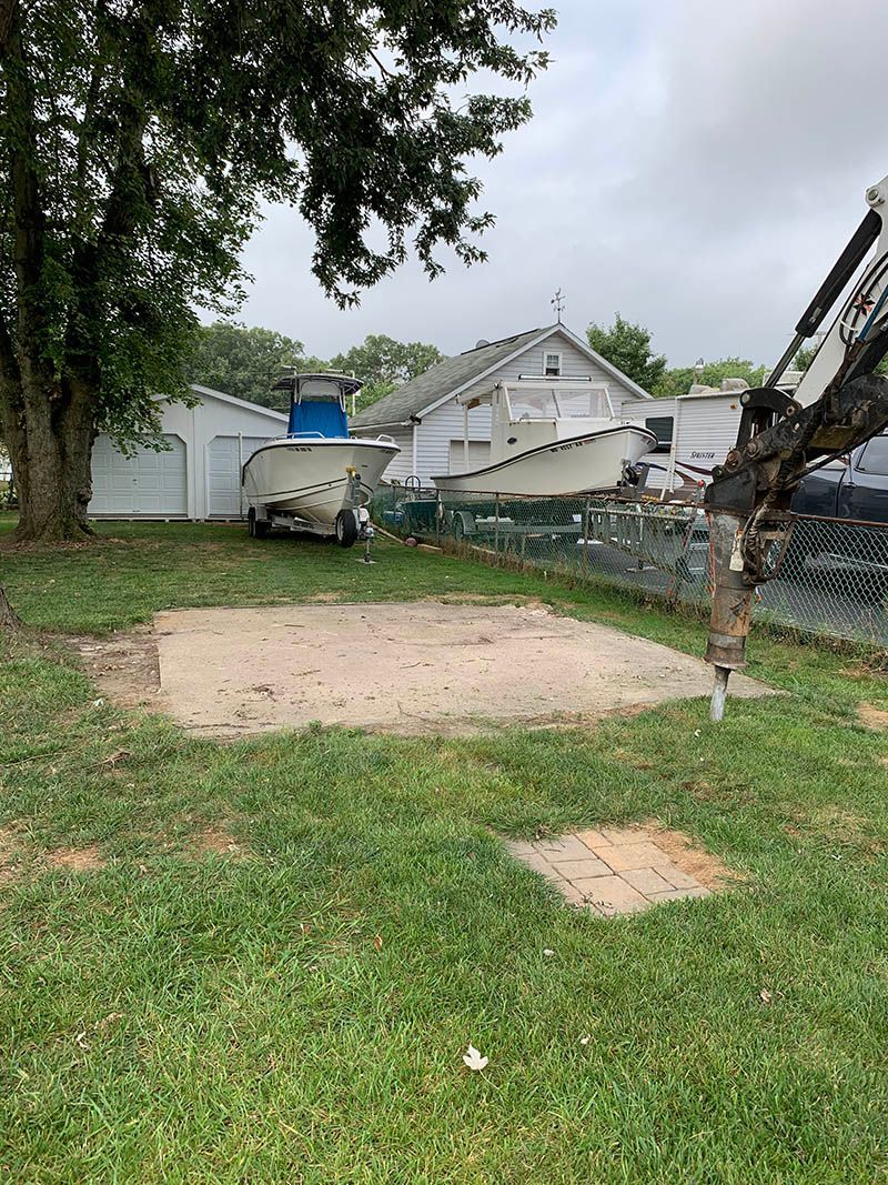 A large excavator is sitting in the middle of a lush green yard in front of a house.
