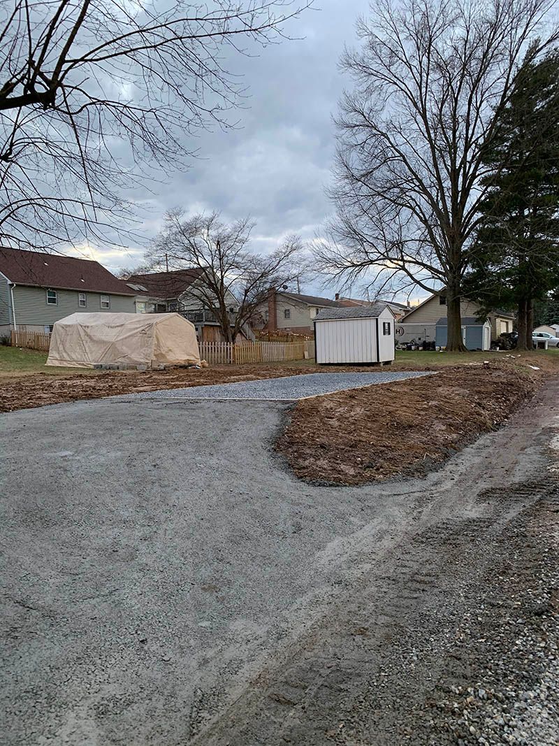 A dirt road leading to a shed in a residential area.