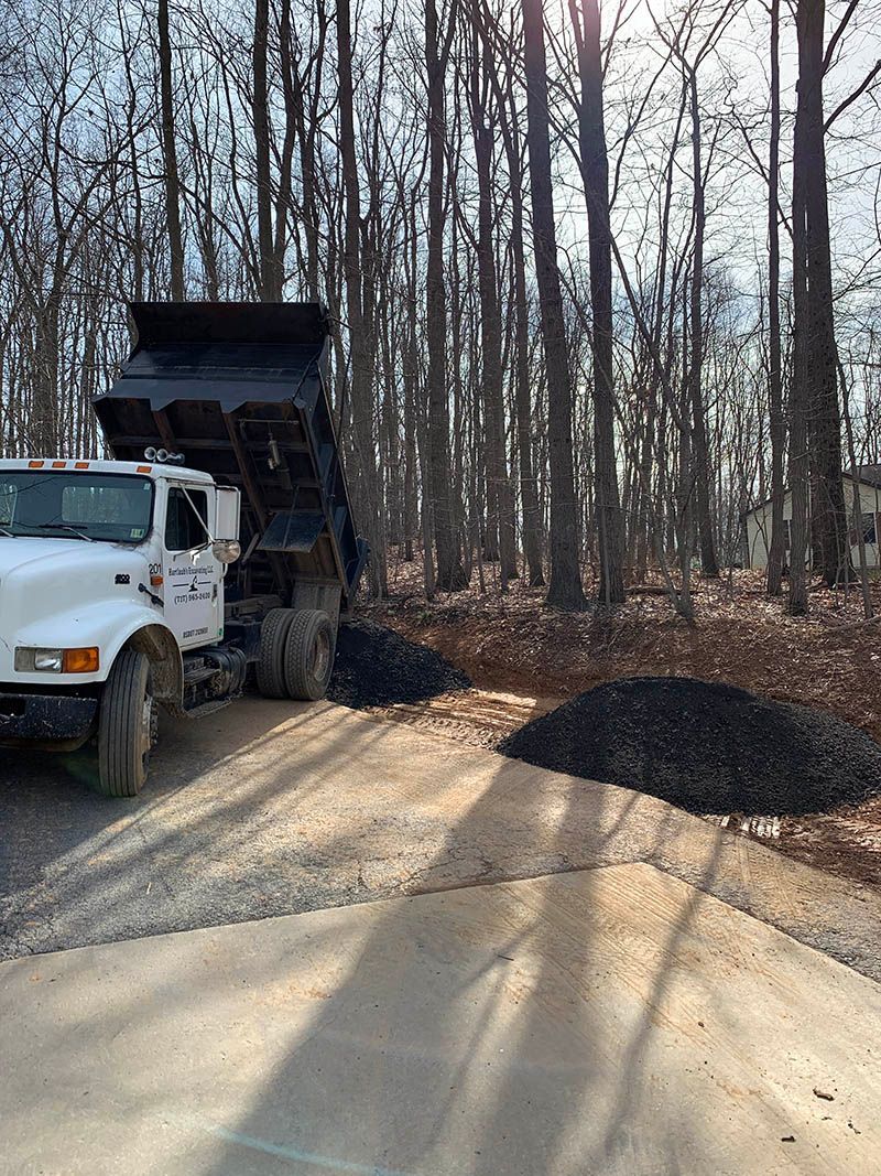 A dump truck is driving down a dirt road in the woods.