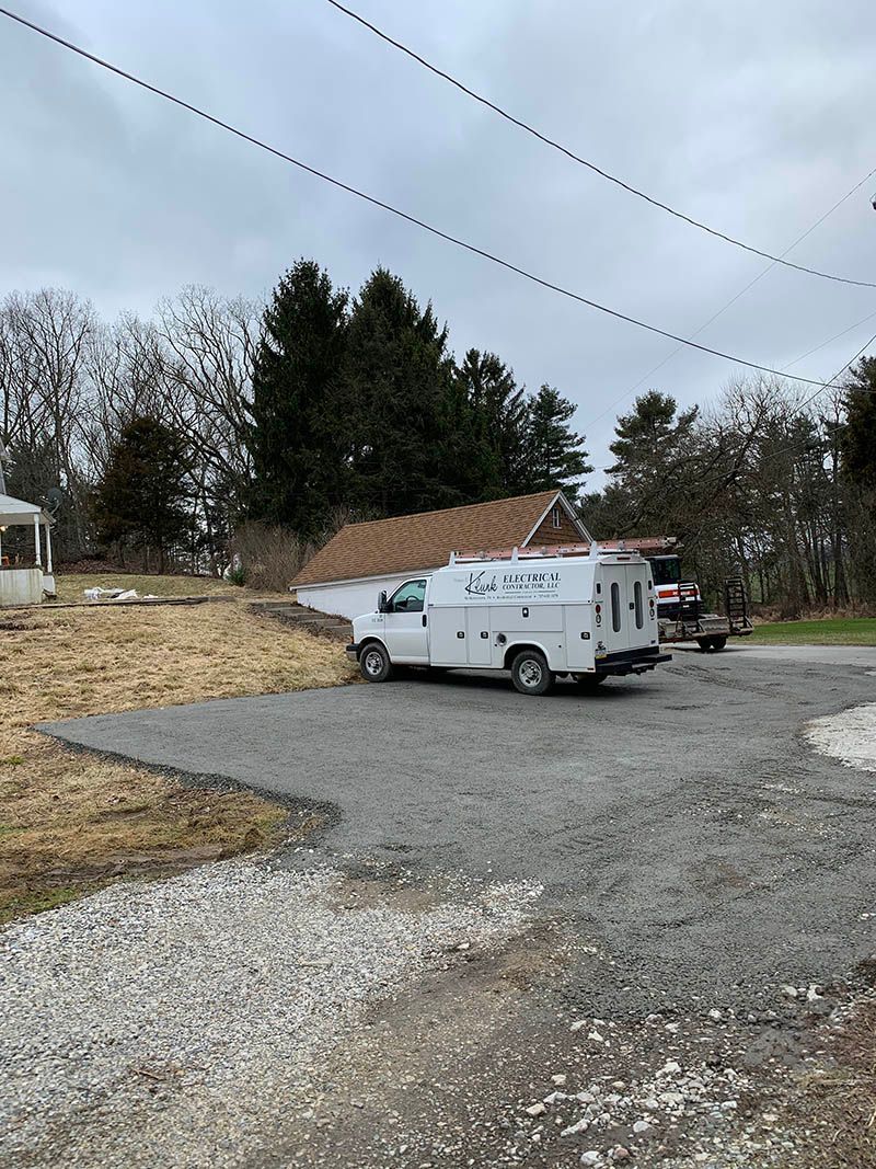 A white van is parked in a gravel lot next to a house.