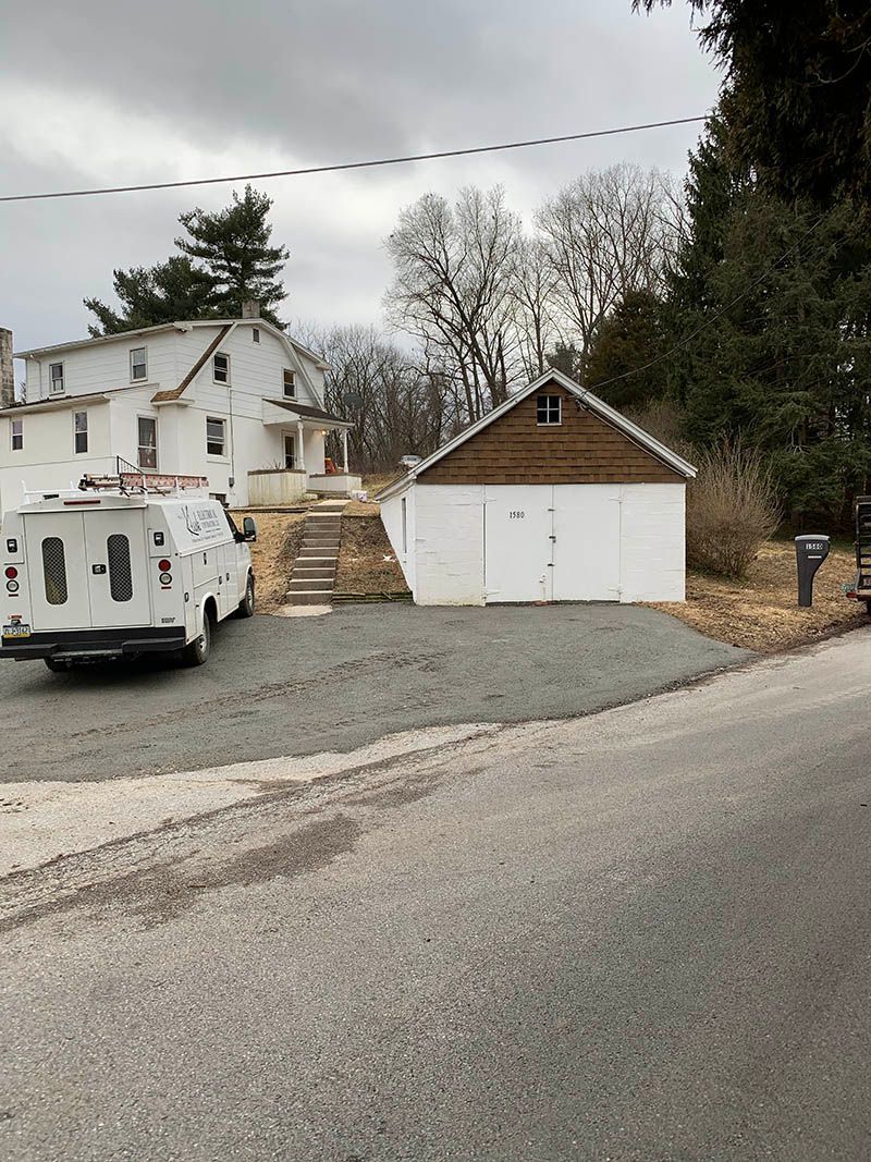 A white van is parked in front of a garage next to a house.