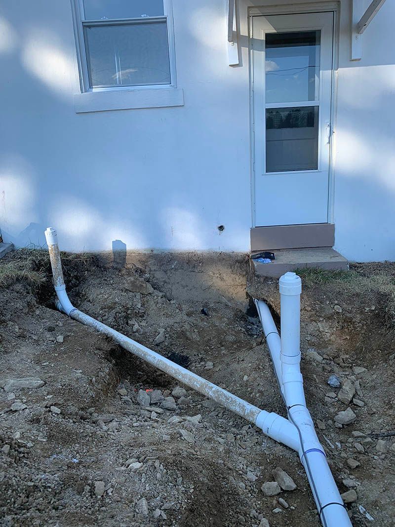 A white house with a lot of pipes in the dirt in front of it.