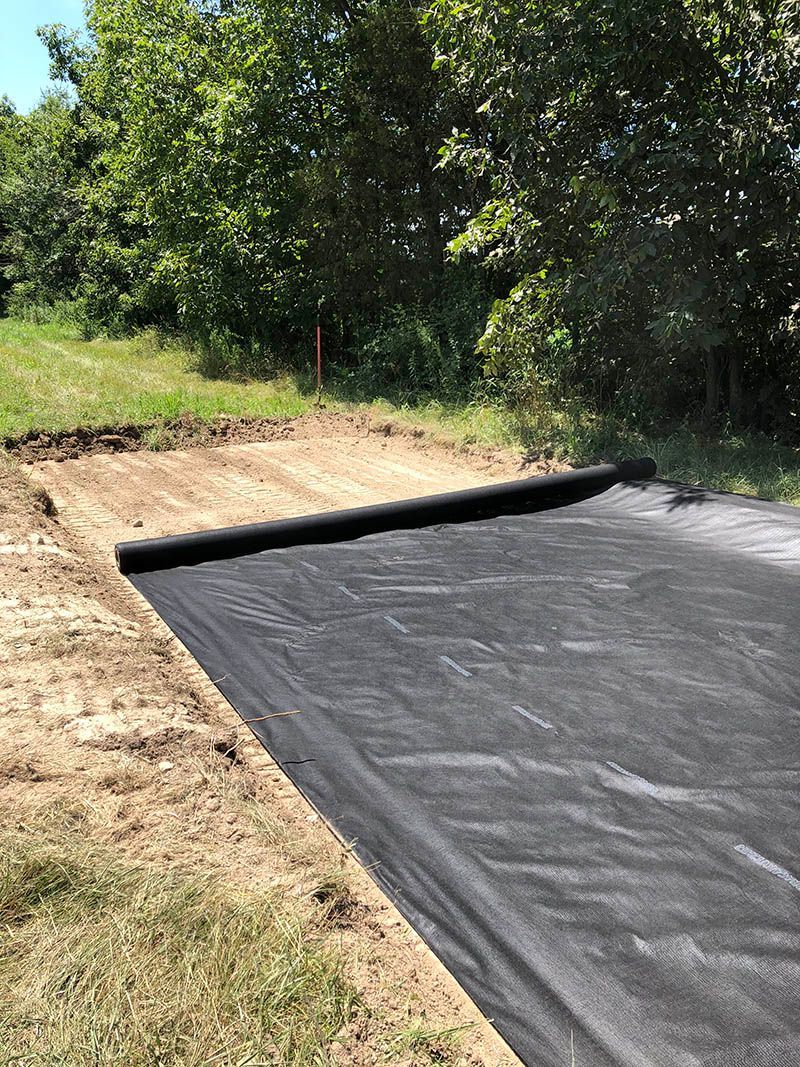 A roll of black weed barrier is sitting on top of a dirt field.