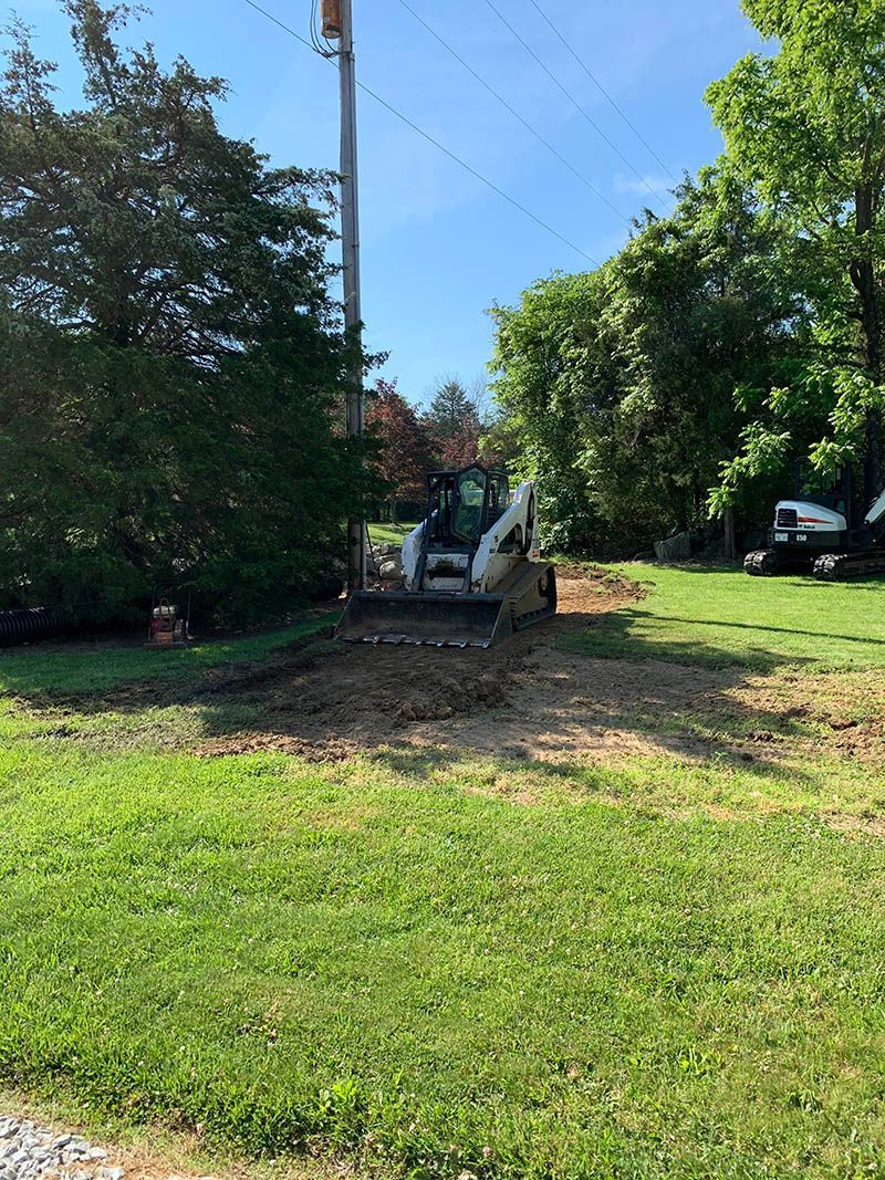 A bulldozer is digging a hole in the grass in a yard.