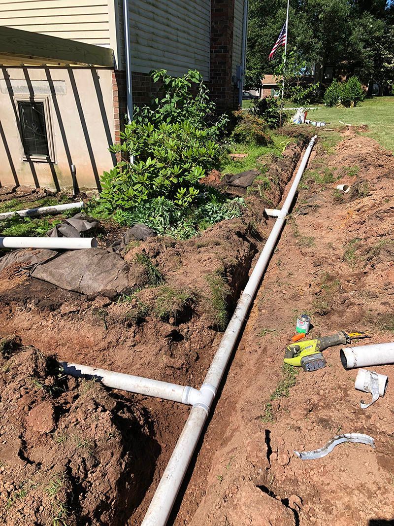 A pipe is being installed in the dirt in front of a house.