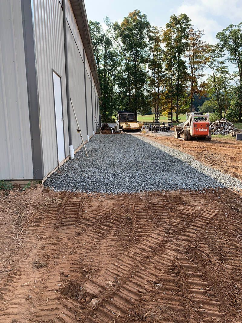 A bulldozer is driving down a dirt road next to a building.