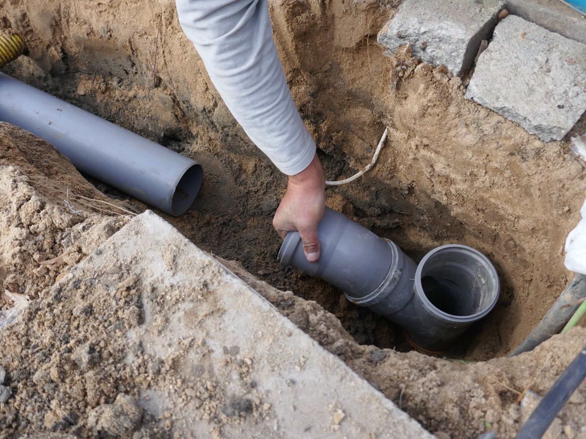 A person is holding a pipe in a hole in the ground.