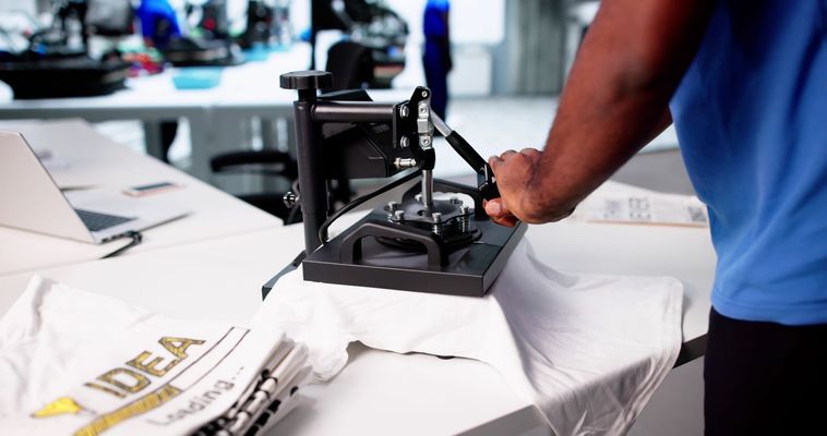 Person using a black heat press on white fabric in a workshop Person using a black heat press on white fabric in a workshop