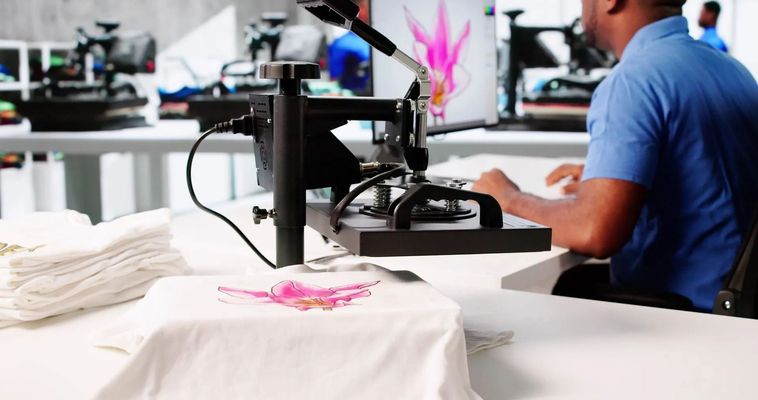 Person operating a printing machine in a workshop, with white shirts and pink prints on the table. Person operating a printing machine in a workshop, with white shirts and pink prints on the table.