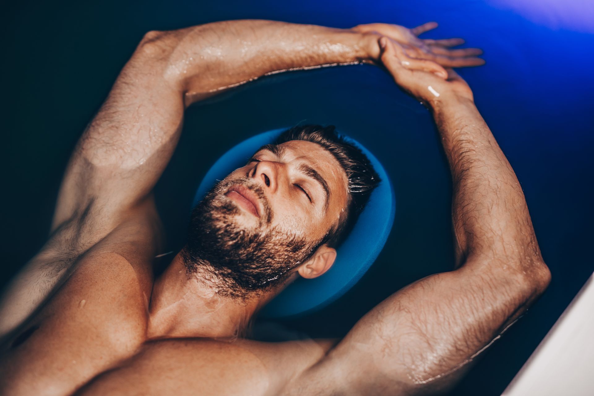 A shirtless man is floating in a bathtub with his arms outstretched.