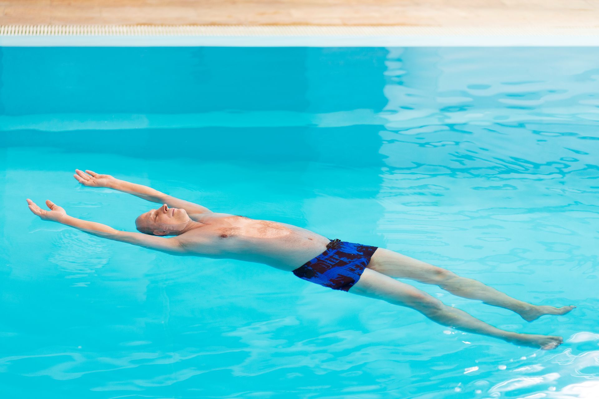 A man is floating on his back in a swimming pool.