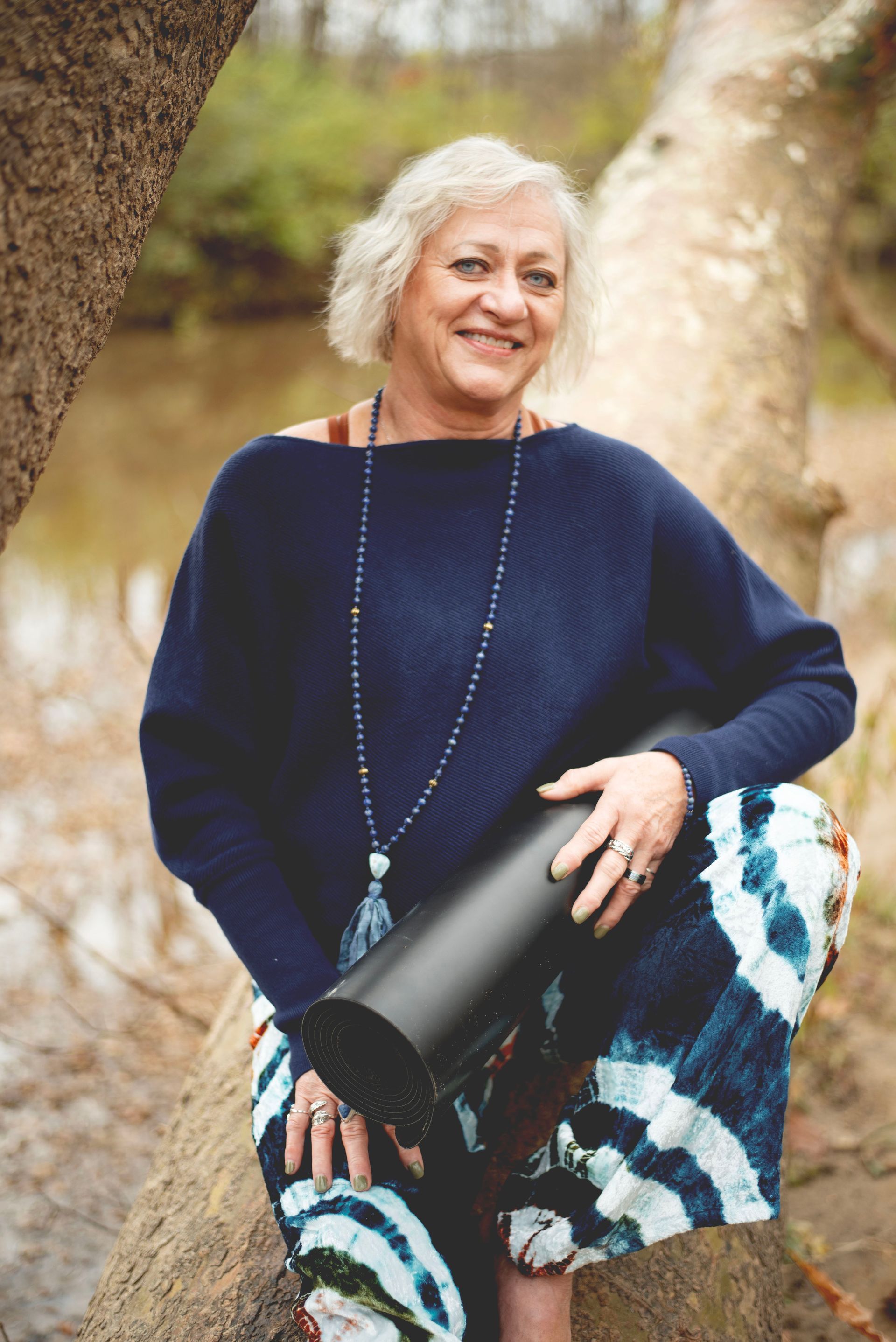 A woman is sitting on a tree branch holding a yoga mat.