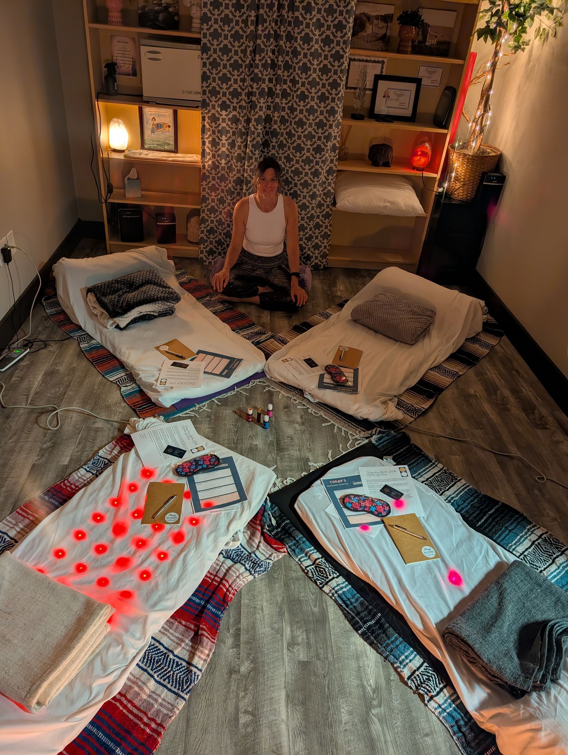 A woman is sitting on the floor in a room surrounded by blankets and pillows.