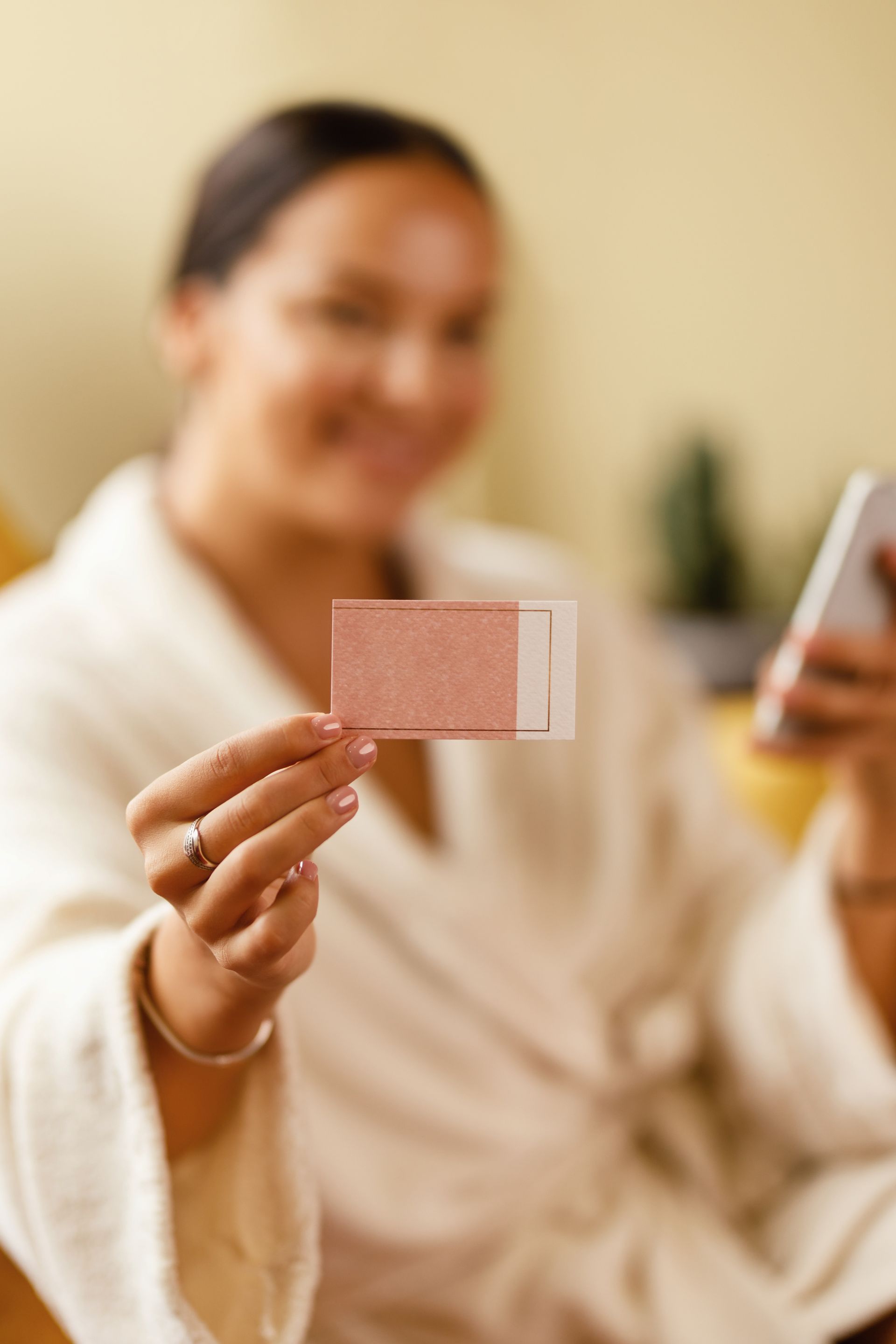 A woman in a bathrobe is holding a card in her hand while looking at her phone.