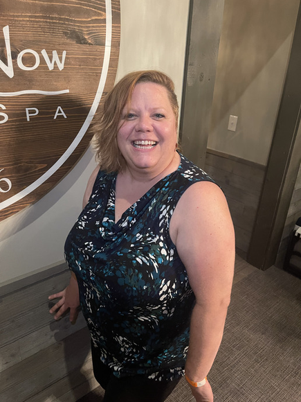 A woman is smiling in front of a sign that says now spa.