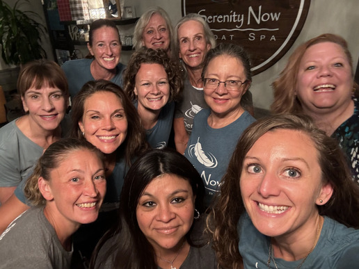 A group of women are posing for a picture in front of a serenity now sign