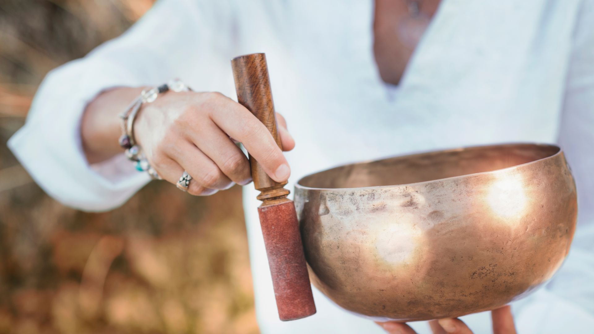 A woman is holding a singing bowl with a wooden stick in her hands.