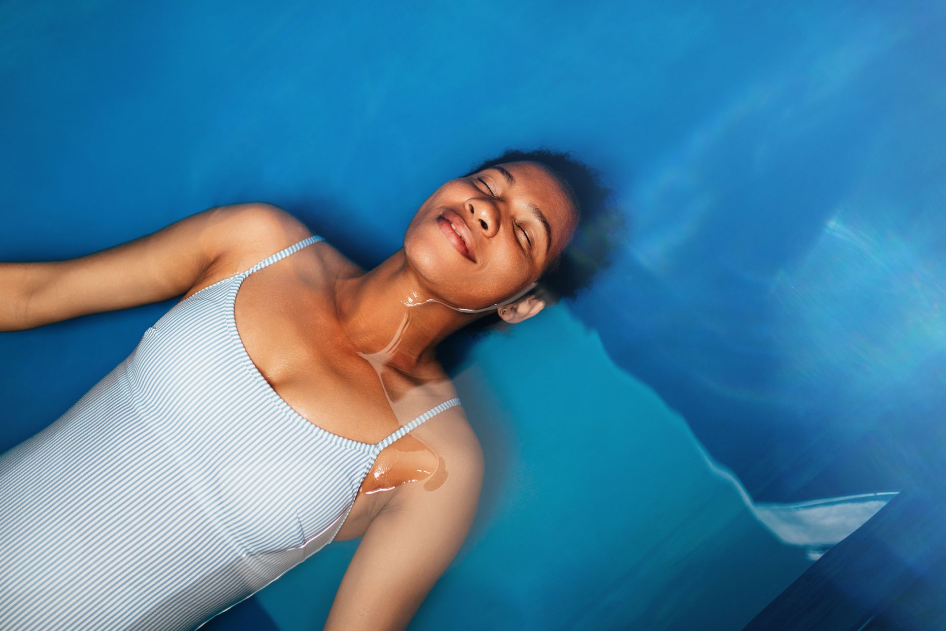 A woman in a white swimsuit is floating in a blue pool.