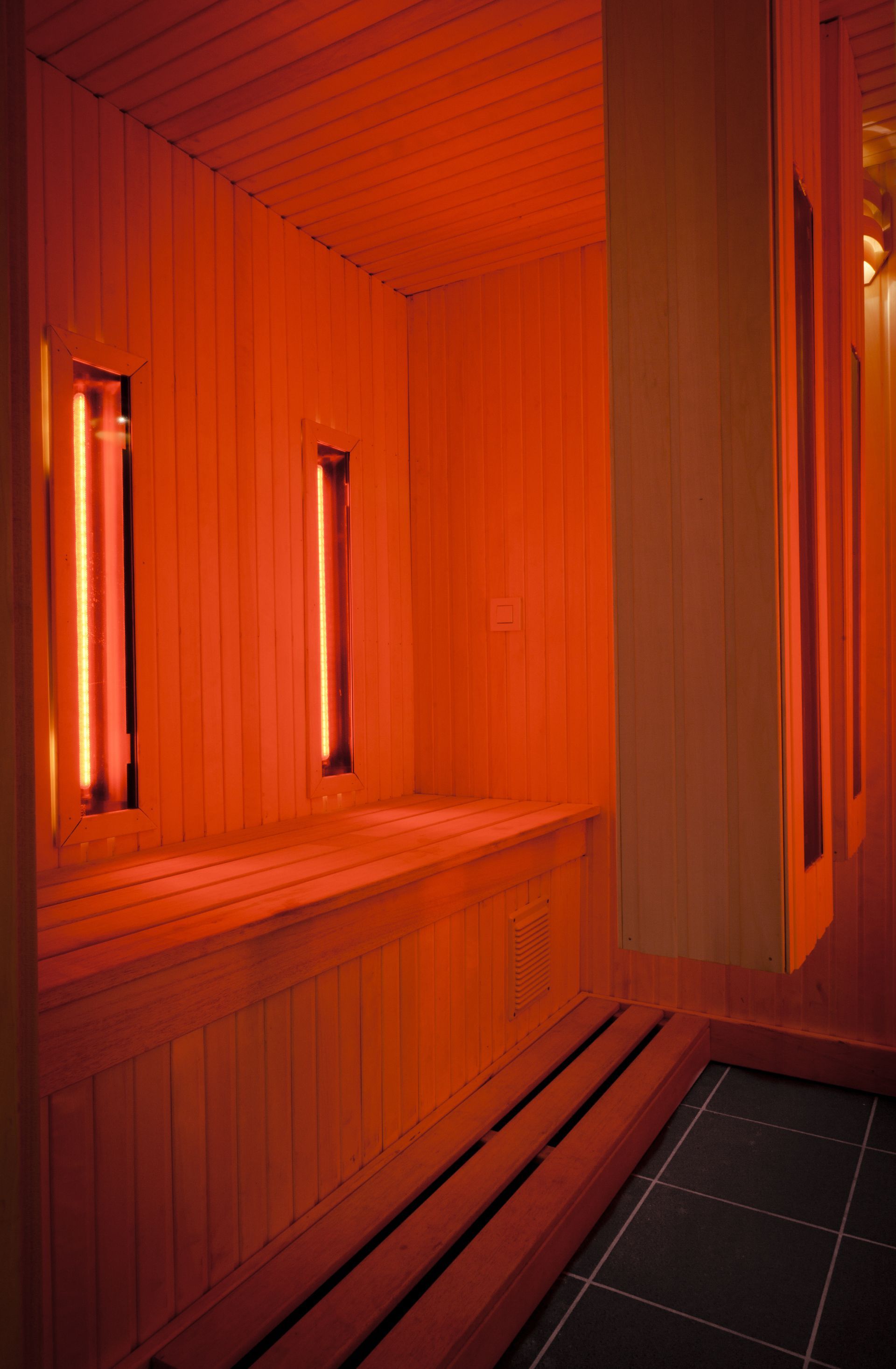 A wooden sauna with red lights on the walls and ceiling.