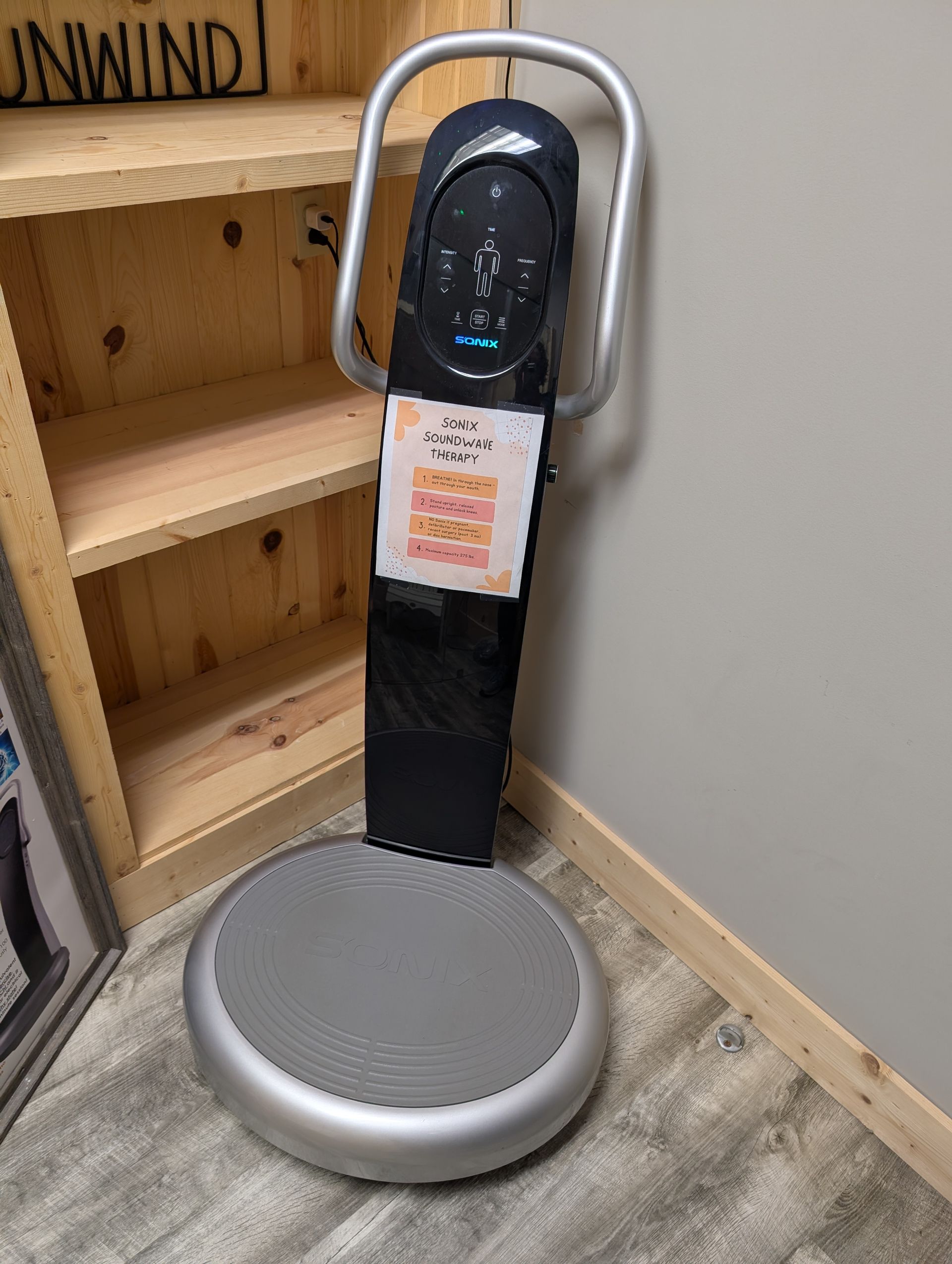 A vibration plate is sitting on the floor in a room next to a wooden shelf.