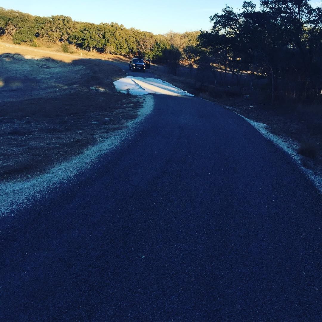 Woman in straw hat smiles, holding wine glass near a lake.