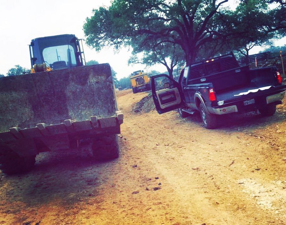 Woman in straw hat smiles, holding wine glass near a lake.