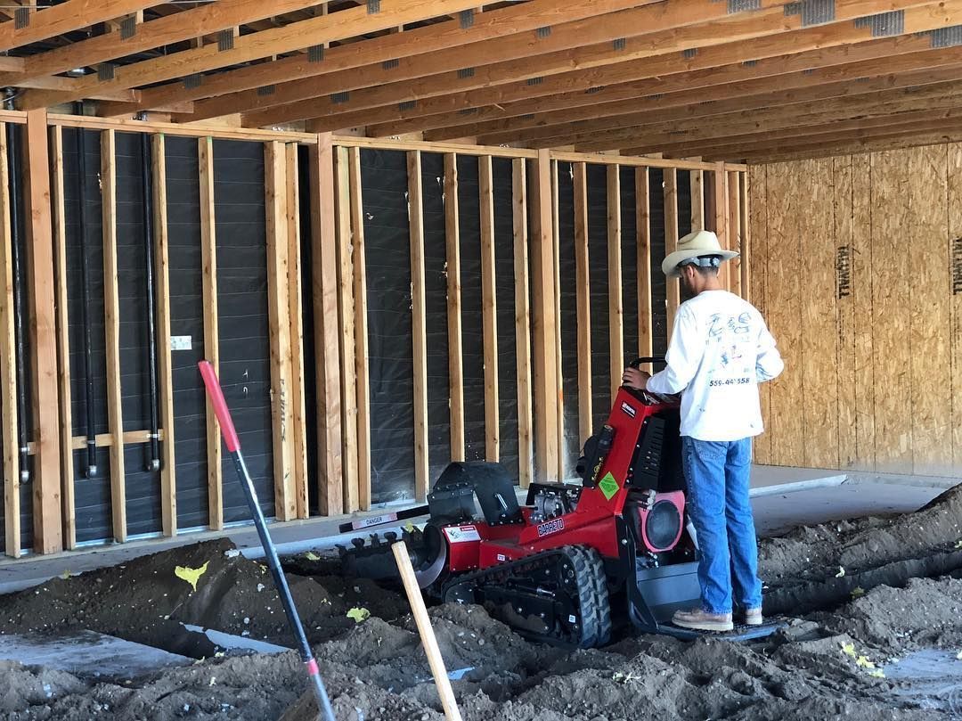 Man operating a red trencher inside a building under construction.