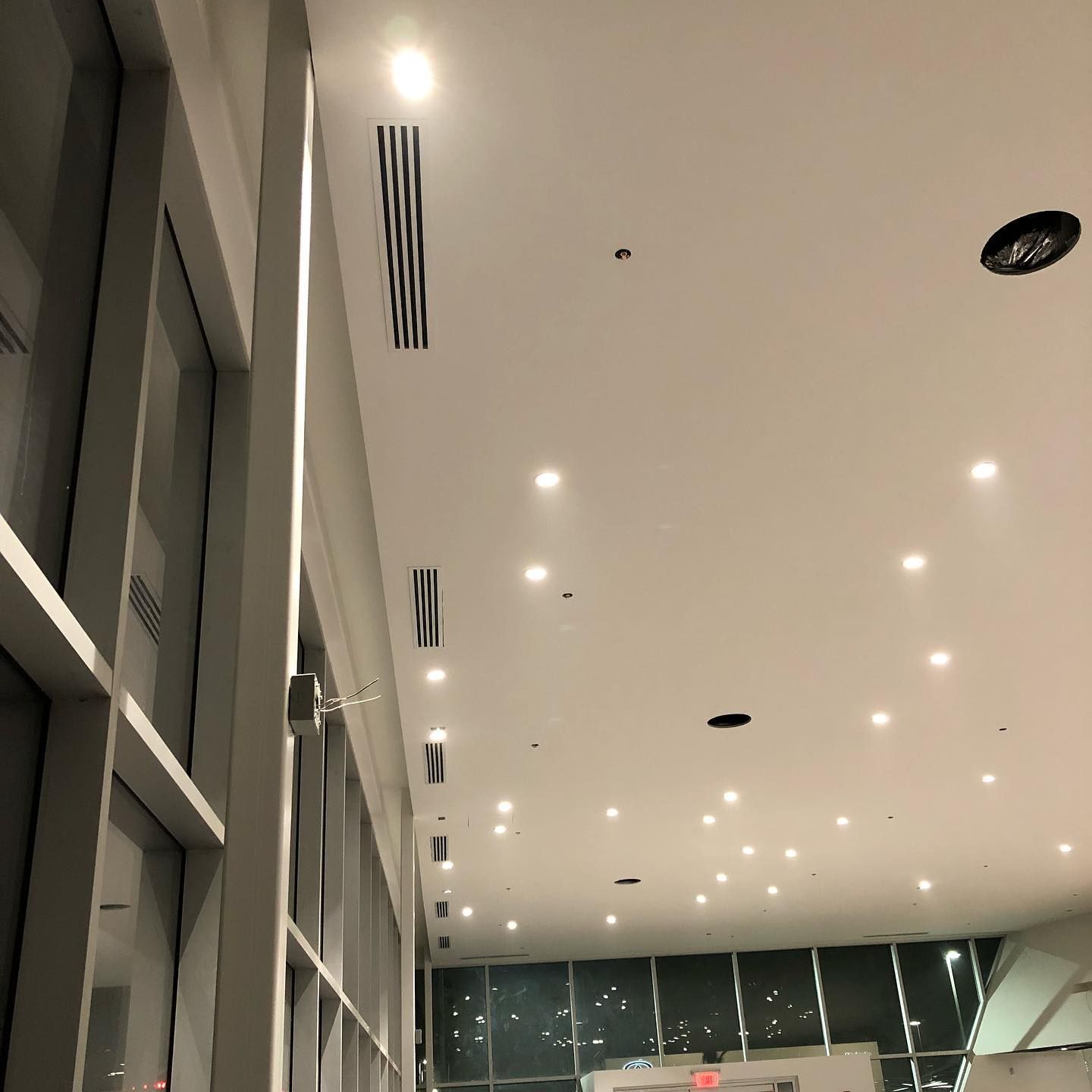 Interior view of a modern building with many ceiling lights. Includes vents and large windows.