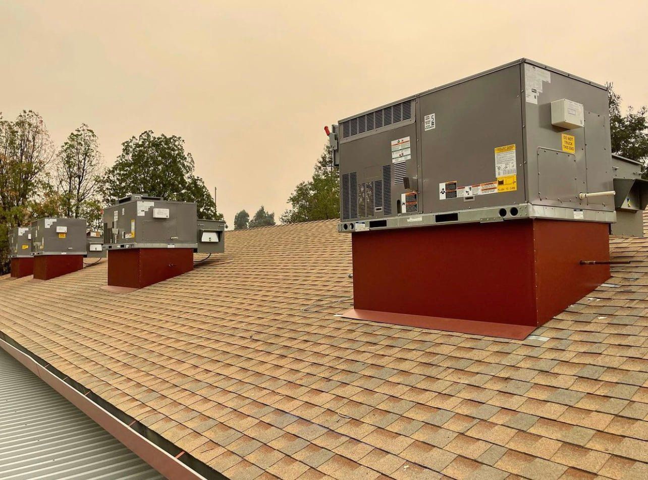 Rooftop with several gray HVAC units on brown-shingled roof with a smoky, hazy sky.