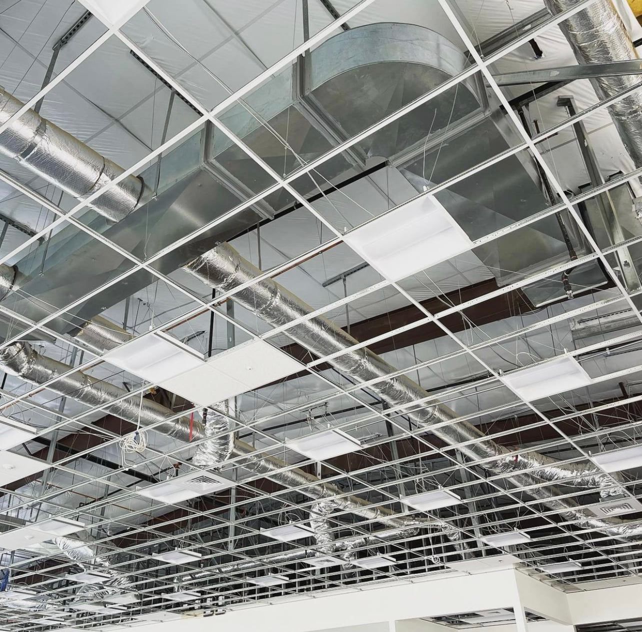 Overhead view of a suspended ceiling with metal grid, air ducts, and recessed lights.