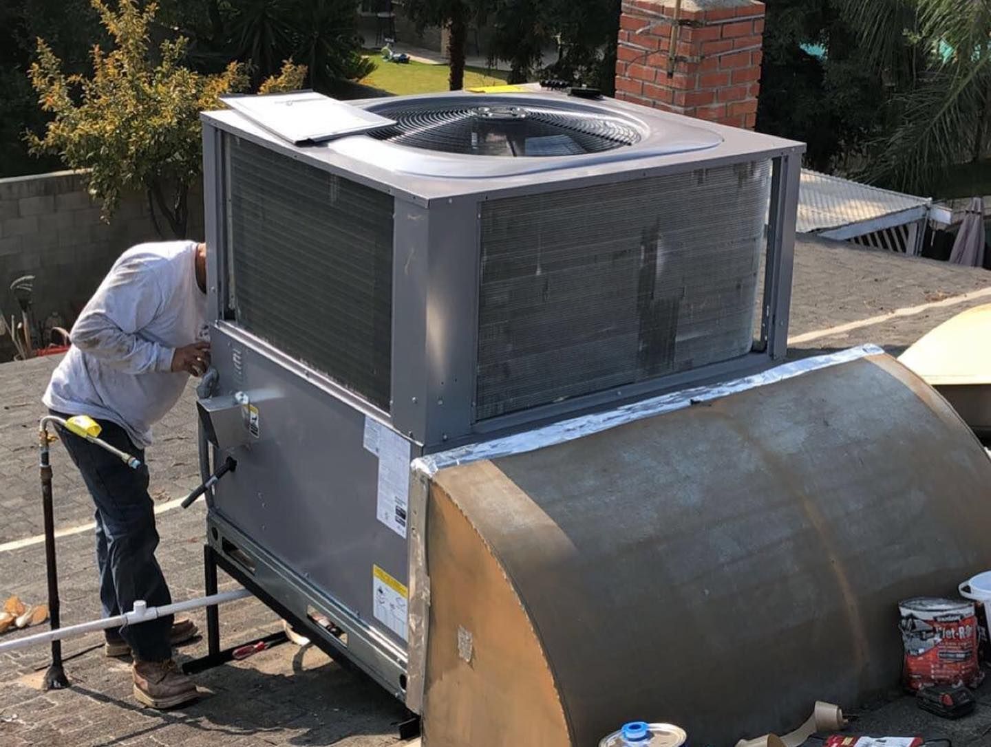 Person in work clothes inspecting rooftop HVAC unit.
