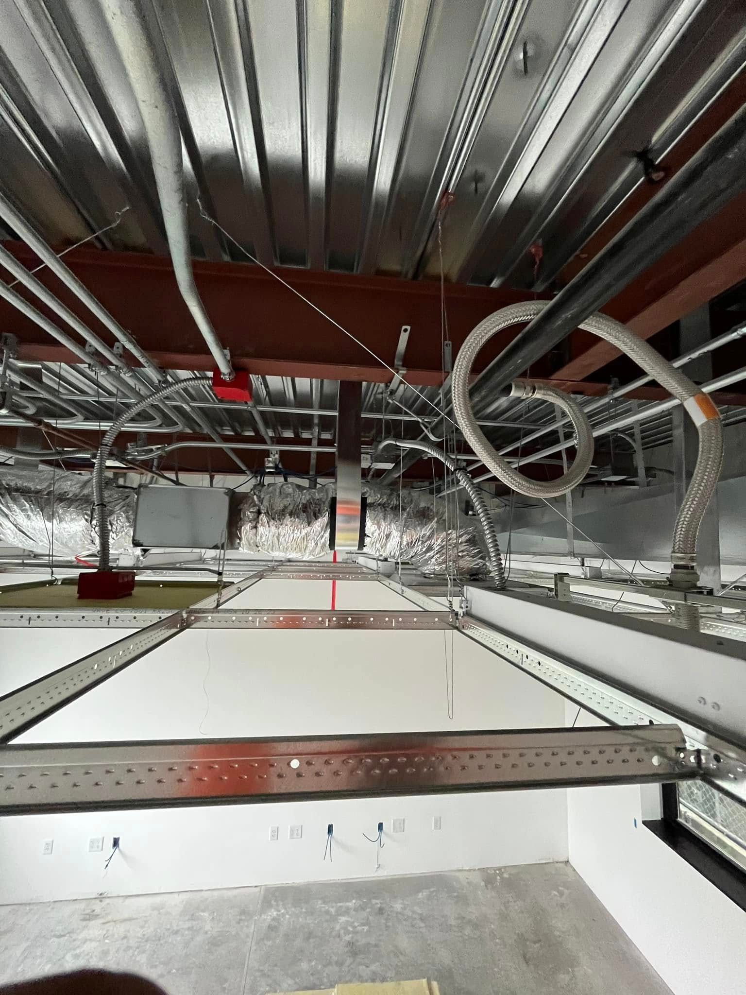 Construction ceiling with metal beams, conduit, and white ceiling tiles.