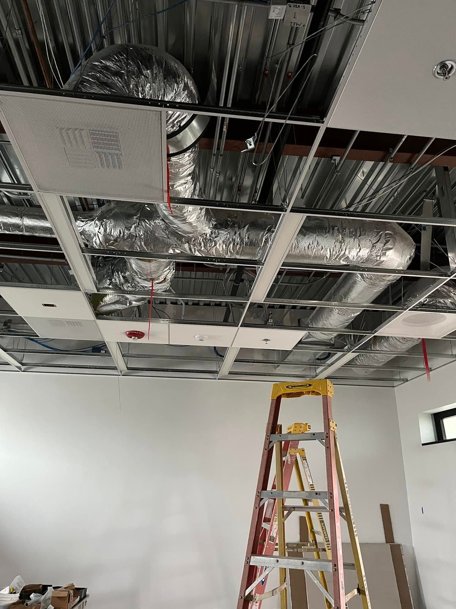 Ladder beneath an unfinished ceiling with ductwork and suspended grid.