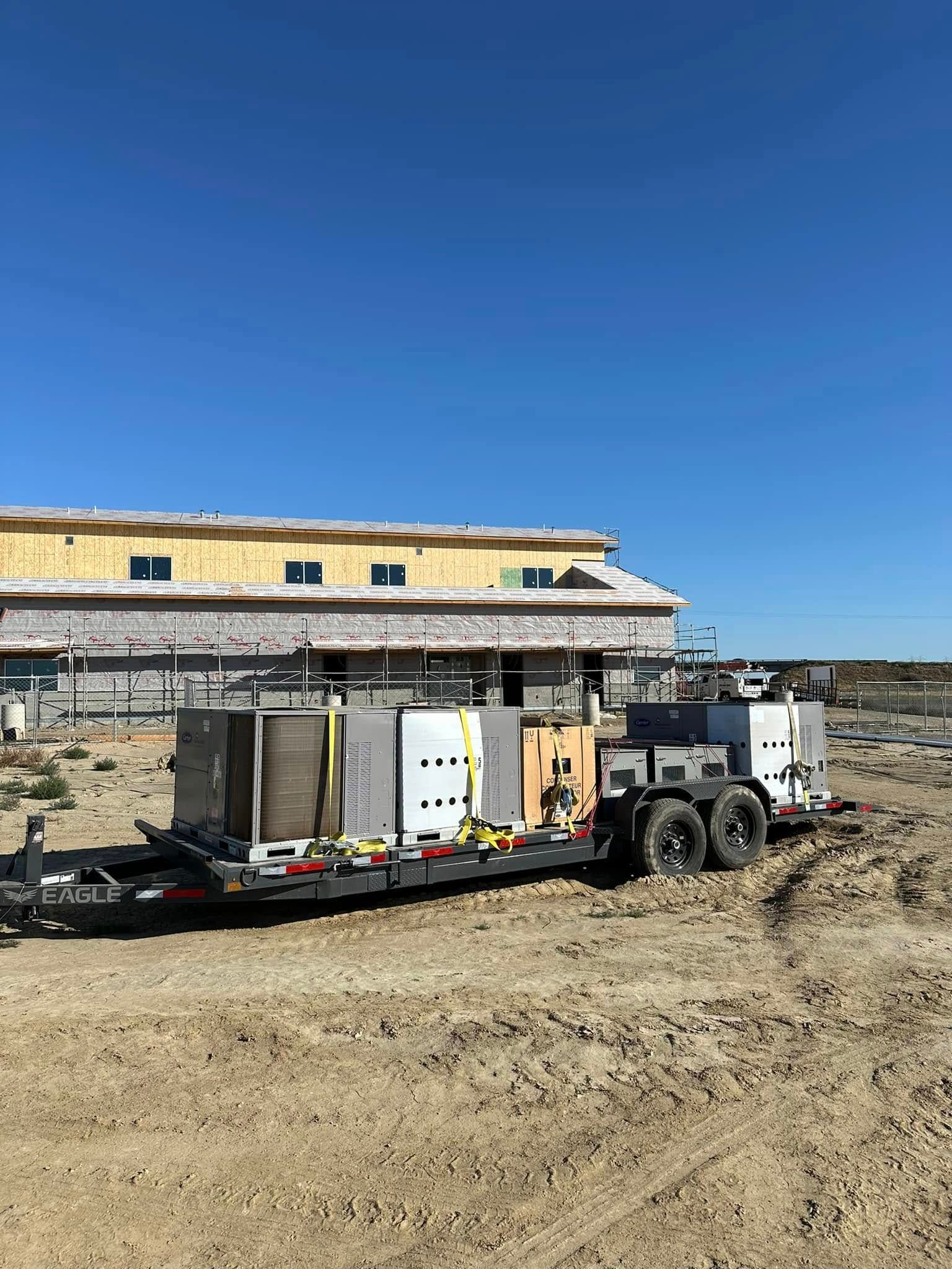 Trailer with equipment at a construction site; building in background under blue sky.