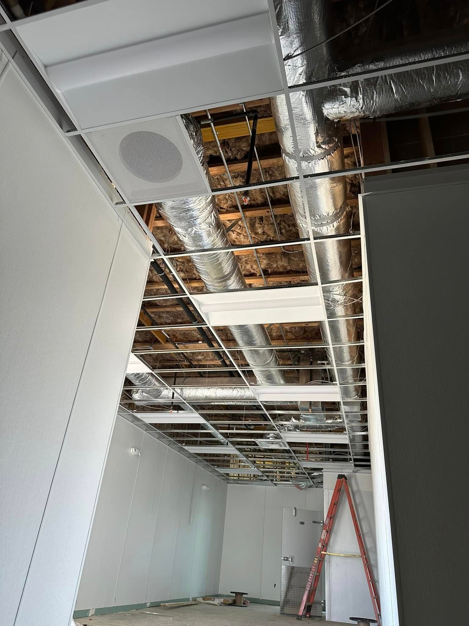Ceiling construction; exposed ceiling joists, ductwork, and partially installed ceiling tiles.