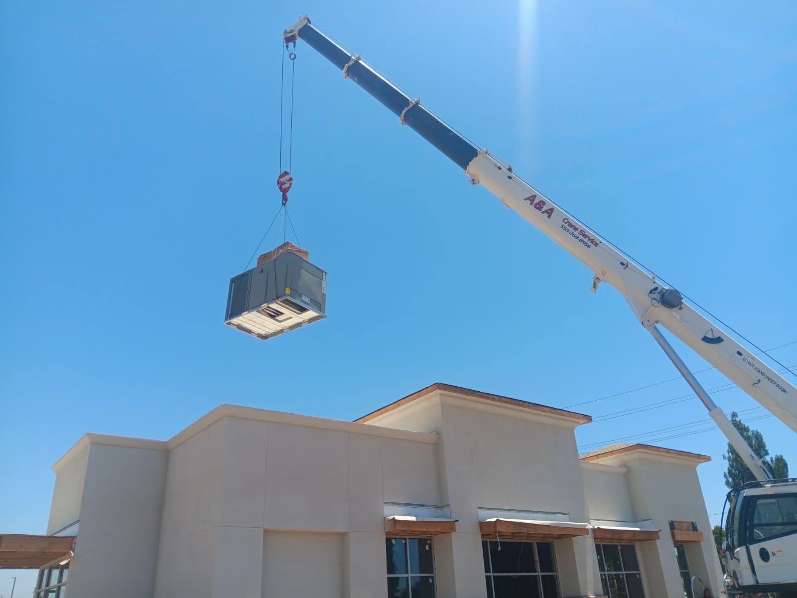 A crane lifting an HVAC unit above a one-story building on a sunny day.
