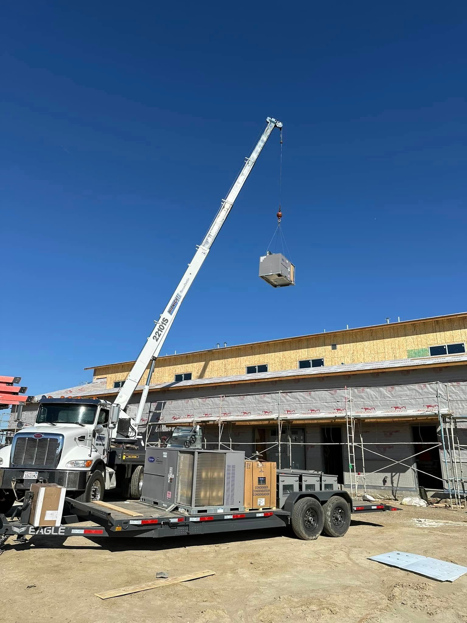 A crane lifting a large HVAC unit onto the roof of a building under construction. Sunny day.