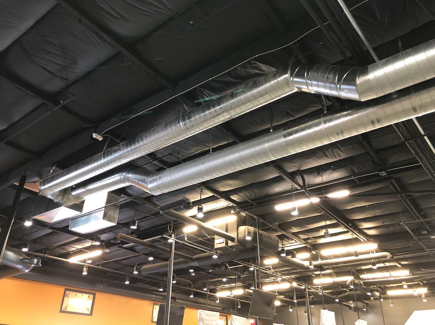 Silver HVAC ductwork on a black ceiling in a commercial space, with recessed lighting.