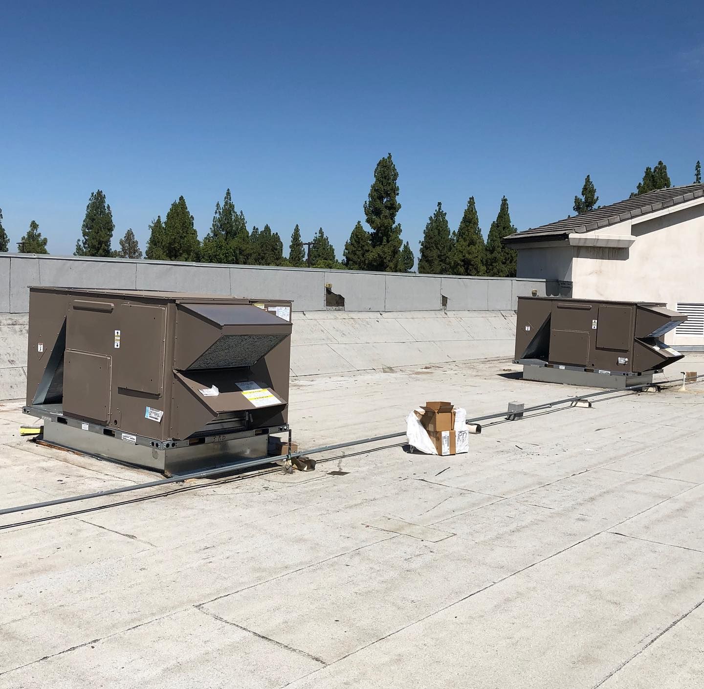 Two brown HVAC units on a flat rooftop. Blue sky and trees in the background.