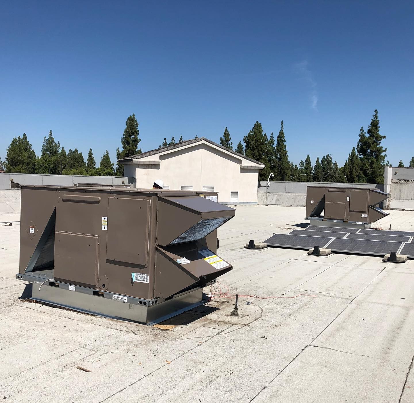 Rooftop with HVAC units on a white surface, blue sky, and trees in the background.